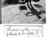 Daily life at Hostel #3, Kunming, China, on a day in February, 1945--Chinese worker carries item on shoulder pole, with  barracks B-5 in the background.