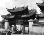 Men waiting near a memorial archway. Local people and architecture in Yunnan province, China, during WWII.