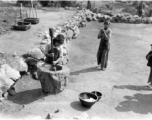 Local children laboring in China, Yunnan province, with a large mortar and pestle, either husking dry grain or mashing cooked rice so something similar. During WWII.