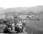 Chinese men eat a banquet, while GIS stand to one side and look at something. The white bands on the heads of some of the men who are eating implies this is a funeral banquet. In China during WWII.