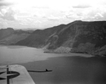 View over wing of Vultee SNV-2 (a variant of the BT-13) trainer piloted by Charles A. Breingan flys over Dianchi Lake (滇池) outside of Kunming, China, during WWII. Small boats dot the water surface, and a large landslide can be seen in the distance. 