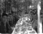 SACO members share a meal with Nationalist soldiers, in the shade of trees, during WWII. In northern China.