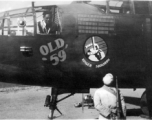 Lloyd Kershaw works in the bombardier's compartment of "Old 59". This B-25C of the 491st Bomb Squadron had completed 221 combat missions, as represented by the 'bomb' symbols painted above the Squadron's ' Ringers' insigne. Kershaw was preparing the aircraft for its trip back to the USA. An unidentified "Old 59" crew member stands beside a Chinese soldier, who would have been guarding the aircraft through the night.