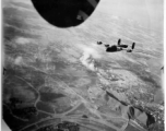 A B-24 flying with smoke billowing up behind from recent bombing, in the CBI, during WWII.