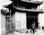 People come and go from village gate in SW China during WWII, with propaganda and military rules posed beside the gate.