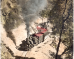 A Darjeeling Himalayan Railway (DHR) B Class 2 ft. saddle tank steam locomotive and train cars climbing the mountain. Hand-tinted image.