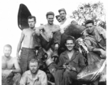 Boys of the 2005th Ordnance Maintenance Company, 28th Air Depot Group, sitting of the engine of a wrecked airplane, in Burma. During WWII. One is holding a puppy--their "mascot" named "Evan." John Schuhart sitting cross-legged with cigarette. 