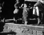 Two toddlers hang out while the adults drink tea at roadside location. In China, during WWII.