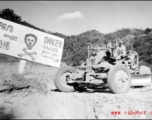 GI driving a road grader next to sign about an extremely dangerous stretch of Burma Road, at 20% grade! In Yunnan, China, or Burma. During WWII.