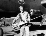 Robert Fox holds a heavy machine gun in front of a B-25 of the Ringer Squadron.
