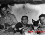 Unknown, Joseph Siana, and Jacob E. Rosencrantz with puppies on bunk in barracks, probably at Yangkai.