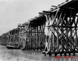 Allies building a wooden trestle bridge across a river in the CBI during WWII.