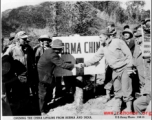 A GI and and a local man shake hands over the China-Burma border, a sign marking that boundary behind them, upon the opening of a road into China. During WWII.