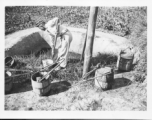 A man collects fertilizer (night soil) from a pit adjacent to farm fields, in preparation for spreading it.