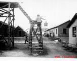 Worker fills water tank at an American base in Yunnan, China, during WWII, by climbing up stairs carrying pails of water.