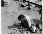 Man does shoe repair with simple tools next to the railway. In India.  Scenes in India witnessed by American GIs during WWII. For many Americans of that era, with their limited experience traveling, the everyday sights and sounds overseas were new, intriguing, and photo worthy.